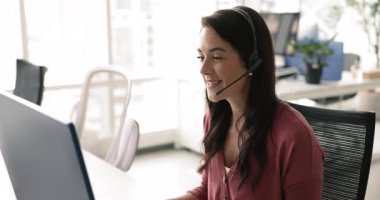 Mutlu Latin müşteri destek operatörü kadın kulaklık takıyor, danışmanlık yapıyor, istemciye talimat veriyor, masaüstü monitöründe sesli konuşma yapıyor, konuşuyor, dinliyor, mikrofonda konuşuyor.