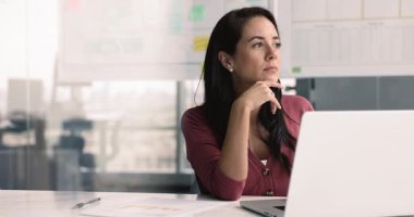 İş yerinde pazarlama stratejisi üzerinde çalışan genç Latin iş kadını, dizüstü bilgisayarla yazı yazan, yüzünü çeviren, çeneye dokunan, iş planı üzerine düşünen, proje yönetimi, yaratıcı fikirler.