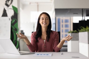 İş ve refahı dengelemek. Huzurlu gülümseyen genç iş kadını elinde defter kağıtlarıyla masamda oturuyor. Parmakları çamurda, rahatlamış ve stresle başa çıkabilmek için derin derin nefes alıyor.