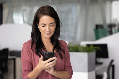 İş bağlantıları. Gündelik kıyafet giyen genç iş kadını, modern ofisteki ortaklarıyla birlikte kalan müşterisiyle telefonda mesajlaşarak dijital ağ oluşturma işine girdi. Boşluğu kopyala