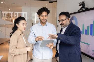 Üç çok ırklı takım arkadaşı, görsel verilere dayanan işbirliği ve analitik iş akışı, takım çalışması ve karar verme mekanizmasına sahip ekran görüntüleme grafiklerinin yanında duran tablet üzerindeki bilgileri tartışır.