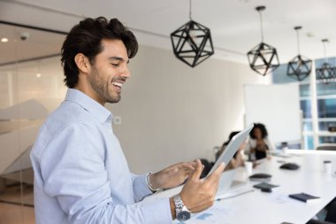 Modern dijital tablet cihazını kullanarak gülümseyen Latin işadamı konferans odasında duruyor, çevrimiçi sunum hazırlıyor, slaytları düzenliyor, takım brifinginden önce içeriği düzenliyor. Uygulama, teknik kullanım