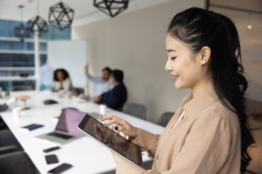 Genç profesyonel Vietnamlı kadın dijital tablet standlarını toplantı odasında tutuyor, uzaktan iletişim kuruyor, içeriği gözden geçiriyor, müşteriler için sunum hazırlıyor, yenilikçi yapay zeka iş teknolojisi kullanıyor.