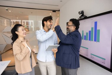 Çok ırklı orta yaşlı ve genç takım arkadaşları beşlik çakıyor, paylaşılan başarının ve takım ruhunun tabletle ofiste bulunuşunu kutluyorlar. Destek, ortak başarılar, verimli takım çalışması
