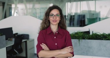 Kendine güvenen, gözlüklü, güven jesti içinde ellerini çapraz yapmış, kameraya bakıp mutlu olan, gülümseyen, kendine güvenen genç, profesyonel bir kadın. Kadın mal sahibi vesikalık fotoğrafı.