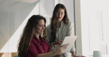 İş yerindeki olumlu bayan meslektaşına dijital tabletle online içerik gösteren mutlu genç ofis çalışanı, profesyonel tavsiye istiyor. Aletle konuşan pozitif kadın iş arkadaşları.