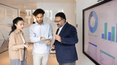 Çeşitli iş adamları modern ofisteki dijital tablet standını kullanarak geniş ekran görüntüleme tablolarının yanına odaklanmış tartışmalara giriştiler. Strateji, performans analizi, yeni işletme uygulaması incelemesi