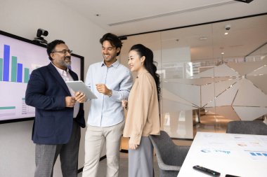 Üç mutlu iş adamı yönetim kurulunda dijital tabletle ekranın yanında durup şema gösteriyorlar, gülümsüyorlar, satış sonuçlarını tartışıyorlar, finansal başarı ve faydaları tartışıyorlar. Takım çalışması, yenilik