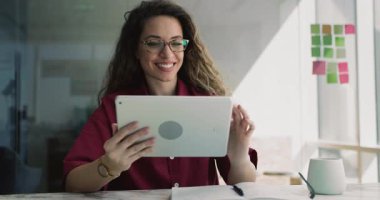 Mutlu genç iş kadını ofis işyerinde internet iletişiminden keyif alıyor, dijital tablet bilgisayarında online servis kullanıyor, video içeriği izliyor, gülümsüyor.