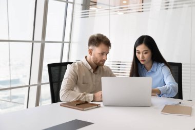 Asyalı ve Kafkasyalı takım arkadaşları dizüstü bilgisayarla ortak görev üzerinde çalışıyorlar, modern yönetim kurulunda buluşuyorlar, verileri gözden geçiriyorlar, bilgileri analiz ediyorlar, işle ilgili sorunları çözüyorlar, fikirleri paylaşıyorlar veya yeni kurumsal yazılım öğreniyorlar.