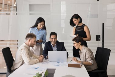 Neşeli ekip konferans odasında dizüstü bilgisayarın etrafında toplandı, işbirlikçi tartışmalara giriştiler, modern cihaz kullanarak olumlu ve üretken takım çalışmalarının tadını çıkardılar, yeni yapay zeka iş yazılımları öğrendiler.