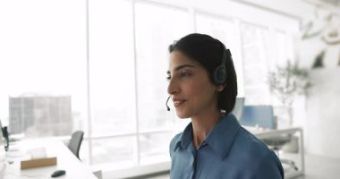 Pozitif dost canlısı genç Latin Destek Merkezi Müdürü kulaklık takmış bir kadın müşteriyle telefonda konuşuyor, mikrofonda konuşuyor, teknik yardım, yardım, danışmanlık yapıyor, monitörü iş için kullanıyor.