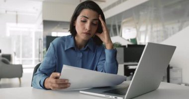 Hayal kırıklığına uğramış genç Latin çalışan kadın ofis işyerinde kötü haberlerle kağıt okuyarak, kovulmak, finansal sorunlar, kariyer sorunları, kafa tutmak, başka tarafa bakmak, düşünmek.