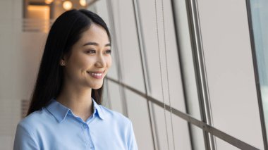 Camdan pencerenin yanında duran güzel Çinli iş kadınının yakın çekimleri iyimser bir ifadeyle dışarıya bakıyor. Kariyer perspektifleri, kişisel başarılar, iş vizyonu ve hırslar