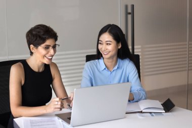 İki çekici çok ırklı kadın meslektaşı dizüstü bilgisayarlarıyla masada oturuyor, yeni online görevi gözden geçiriyorlar, yaklaşan sunum veya toplantı için ayrıntıları kesinleştiriyorlar, şirket ofisinde verimli bir takım çalışmasının keyfini çıkarıyorlar.