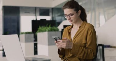 İş yerinde akıllı telefonlara yazı yazan, iş iletişimi için mobil internet uygulaması kullanan, iş yerinde dizüstü bilgisayarla oturan, gözlüklü profesyonel bir kadın.