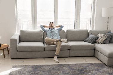 Bağımsız hayatın rahatlığı. Huzurlu mutlu milenyum adamı rahat kanepeye uzanıp gülümseyerek el ele tutuşarak rahat aydınlık oturma odasında stres atarak huzurlu bir hafta sonunun tadını çıkarıyor.