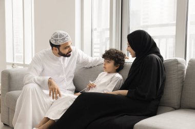 Ebeveyn rehberliğinde açık iletişim. Geleneksel Müslüman ailelerin ilgilendiği genç bir Arap aile, okul çocuğu ebeveynleri giyer. Kanepeye oturur, çocuklarla konuşur, oğluyla okul meselelerini tartışır.