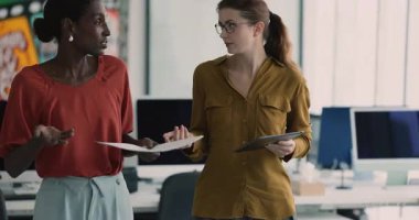Ofiste yürüyen iki ciddi kadın iş arkadaşı sorun çözmeyi tartışıyor, tablet ve belgelerde yanlış veriler var, pazarlama raporları hakkında tartışıyorlar.