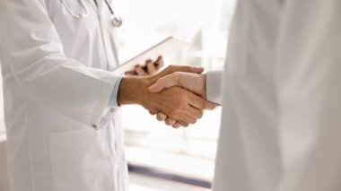 Laboratuvar önlüklü iki doktor el sıkışıyor. Erkek pratisyenler, iş birliği, ortaklık ve birlikte çalışma nedeniyle tokalaşan tıp uzmanları. Kırpılmış afiş atışı