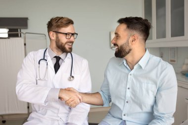 Neşeli genç Latin hasta erkek doktorla el sıkışıyor tıbbi yardım, destek, danışma, başarılı terapi, gülümseme, kahkaha için teşekkür ediyor. Muayene odasında doktor el sıkışıyor.