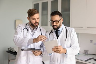 Odaklanmış İspanyol doktor iş arkadaşından yardım, tavsiye, profesyonel destek istiyor, hastanın elektronik kayıtlarını dijital tabletten meslektaşına gösteriyor. İki doktor teşhisi tartışıyor