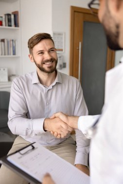 Başarılı bir konsültasyondan sonra doktor ile tokalaşan mutlu genç erkek hasta güven, minnettarlık ve gülümseme hissediyor. Klinikteki pratisyen hekimle el sıkışan genç adam.