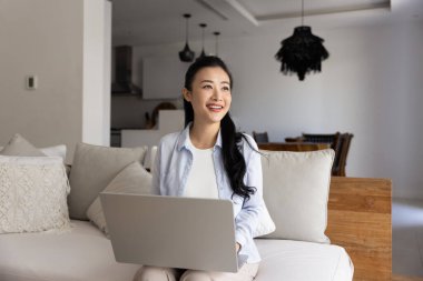 Uzaktan bilgisayar kullanarak gülümseyen Asyalı kadın internette geziniyor, çalışıyor ya da evdeki rahat kanepede oturarak online kurs alıyor. Modern yenilikçi yapay zeka kullanımı iş, öğrenme veya eğlence için
