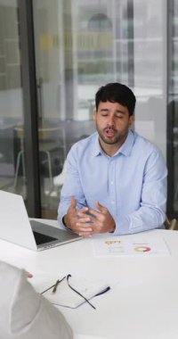 Genç İspanyol işadamı, modern ofiste masa başında oturmuş, satış sonuçlarını ve ilerlemeyi sunuyor, proje güncellemelerini sunuyor, meslektaşlarına yeni bir fikir veya strateji öneriyor