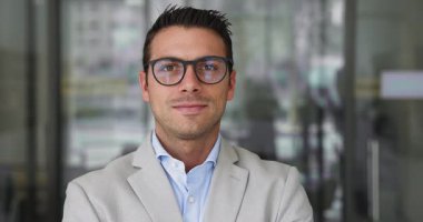 Resmi takım elbise giymiş gülümseyen profesyonel Latin iş adamının yakın portresi. Gözlük takıyor, neşeli bir ifadeyle kameraya bakıyor, makama güvenle bakıyor, yetkinlik ve otorite yayıyor.