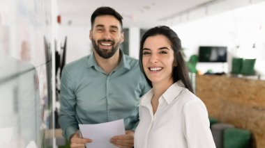 İki genç profesyonel gülümsüyor, modern çalışma ofisinde birlikte poz veriyorlar, planlama, üretken, pozitif takım çalışması, coşkulu bir güven, iş akışında başarı.