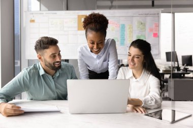 Üç neşeli yaratıcı profesyonel, pazarlama departmanı üyeleri, dizüstü bilgisayar, beyin fırtınası sezgileri, yeni kampanya, hizmet veya ürün fikirlerini paylaşarak ofiste bir araya geldiler. Takım çalışması.