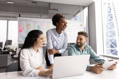 İş yerinde laptop ve modern tablet aygıtı kullanarak olumlu iletişimde bulunan üç takım arkadaşından oluşan bir grup, şaka sırasında gülerek çağdaş yüksek katlı ofis binasında toplanıyor. Takım çalışması.