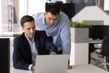 İki odaklanmış takım üyesi birlikte çalışıyor, dizüstü bilgisayar kullanarak görevleri, zaman çizelgelerini veya projedeki ilerlemeyi kontrol ediyor, ürün veya web sitesi için görsel kavramları gözden geçiriyor, çalışmalarıyla ilgili yeni beceriler öğreniyor