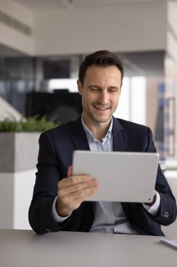 İşle ilgili yeni yapay zeka platformu, web sörfü bilgileri, elektronik hizmetleri veya yönetim uygulamaları kullanarak, modern işyerindeki masada oturmuş dijital tablete yazı yazan neşeli yönetici