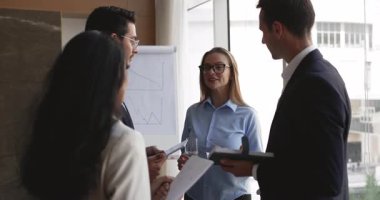 Dört başarılı genç iş arkadaşı ofis yönetim kurulunda konuşuyor, birlikte duruyor, beyin fırtınası yapıyor, takım çalışması için yaratıcı fikirleri tartışıyor, iletişim kuruyor.