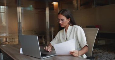 İş yerindeki kağıt para raporlarını kontrol eden, dizüstü bilgisayarda yazan, muhasebe işi için çevrimiçi ebank başvurusunu kullanan, şık gözlükler takan, ciddi beyaz iş kadını.