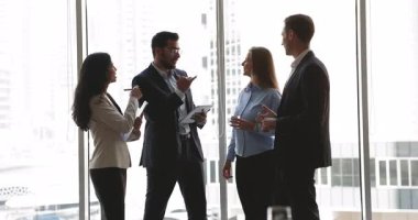 Dört şirket meslektaşından oluşan çeşitli ekip iş molasında sohbet ediyor, arka planda şehir manzarası olan büyük ofis penceresinde duruyor, konuşuyor, gülüyor, eğleniyor, eğleniyor, çevrimdışı iletişim kuruyor, ağ kuruyor.
