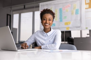 Gülümseyen Afrikalı iş kadını, proje yöneticisi, iş analisti veya pazarlama stratejisti portresi ofiste dizüstü bilgisayarda çalışıyor, planlama, koordinasyon görevleri, uzak iş akışı