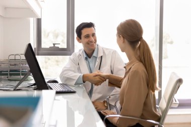 Neşeli, yakışıklı İspanyol doktor hastane ofisinde kadın hastayla el sıkışıyor, gülümsüyor, gülüyor, mükemmel sağlık için tebrik ediyor, sağlık kontrolünden sonra iyi tıbbi test sonuçları.