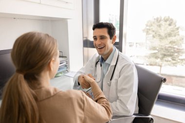 Mutlu genç İspanyol doktor klinikte çalışan sağlıklı bir kadına sağIıklı bir şekilde el sıkışırken gülümsüyor, gülüyor, konsültasyonu bitiriyor ve iyileşme sürecini başarıyla tartışıyor.