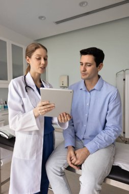 Elektronik sağlık raporunu açıklayan genç bir kadın doktor, erkek hastaya tablet üzerinde iyi bir test sonucu gösteriyor, tavsiye veriyor, ziyaretçi doktor ofisine internet üzerinden reçete yazıyor.