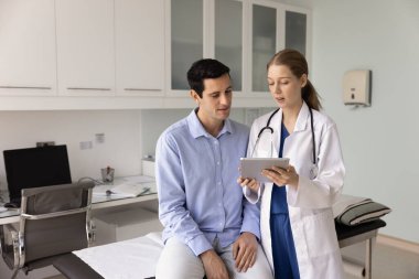 Genel pratisyen kadın, tıbbi kanepede oturan genç erkek hastaya muayene sonucu gösteren, sağlık raporlarını açıklayan, konsültasyon yapan, tavsiye veren,