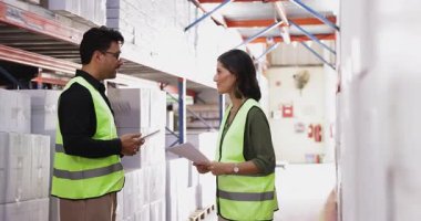 Depoda duran koruyucu yelekli iki Latin depo çalışanı ellerinde belgeler ve dijital tabletle el sıkışma, güven jesti, anlaşma, etkili takım çalışması gibi konuları sonuçlandırdılar.