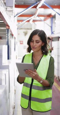 Depoda dijital tablet kullanarak çalışan, envanter verilerini kontrol eden, güncelleyen, hisse senedi kayıtlarını yöneten veya ürün detaylarını denetleyen 30 'lu yaşlardaki güvenlik yeleği giyen genç İspanyol kadın.