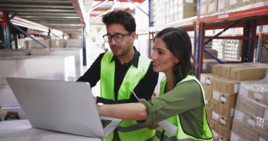 Depoda duran meslektaşlar dizüstü bilgisayar kullanarak lojistik veya envanterle ilgili verileri analiz ediyor, sevkiyat veya hisse senedi raporlarını inceliyor, ürün bilgilerini tartışıyor, depolama organizasyonu üzerinde işbirliği yapıyor.