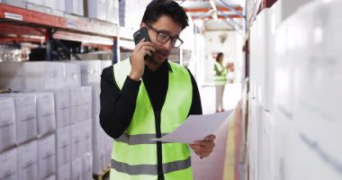 Hispanik erkek, depo ya da lojistik koordinatörü güvenlik yeleği giymiş envanter verileri, nakliye ya da akıllı telefondan tedarik zinciri operasyonlarını tartışıyor. Depo, dağıtım merkezi iş akışı