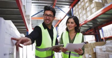 Sevkiyat veya envanter detaylarını inceleyen iki tedarikçi, ürün verilerini doğrulayan, karton kutularla dolu raflarla çevrili büyük depo lojistik merkezinde birlikte çalışan
