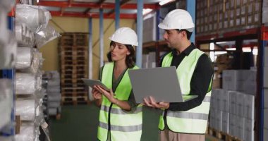 Depo koridorunda ayakta dikilip tablet ve dizüstü bilgisayar kullanarak stok ve envanter denetiminde işbirliği yapan iki İspanyol iş arkadaşı. Lojistik, takım çalışması
