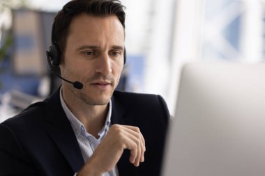 Orta yaşlı İspanyol bir adama yakın çekim, çağrı merkezi çalışanı kulaklık takıyor ve müşteriye uzaktan yardım etmekle meşgul olan bilgisayar ekranına bakıyor. İletişim ve profesyonel destek hizmeti